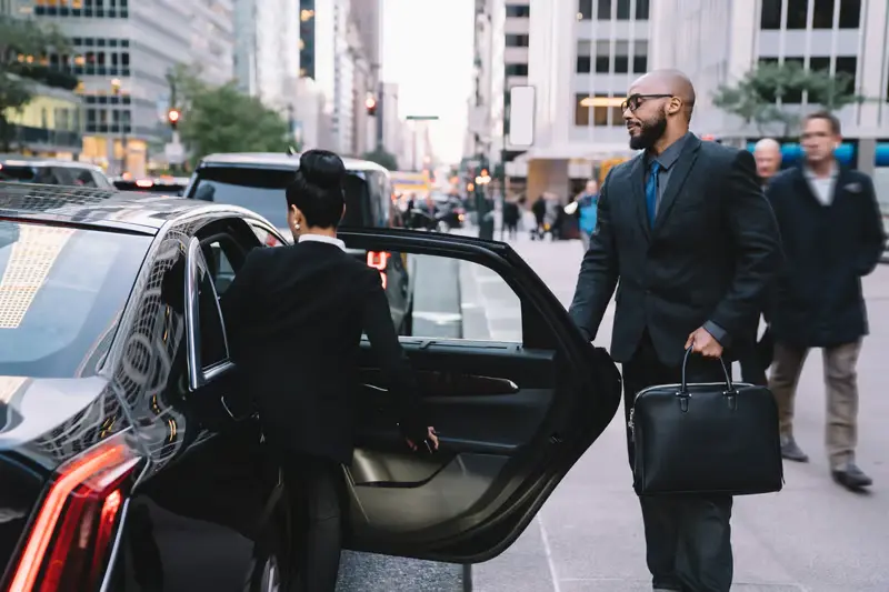 Chauffeur opening a car door for a businessman on a city street — Chicago